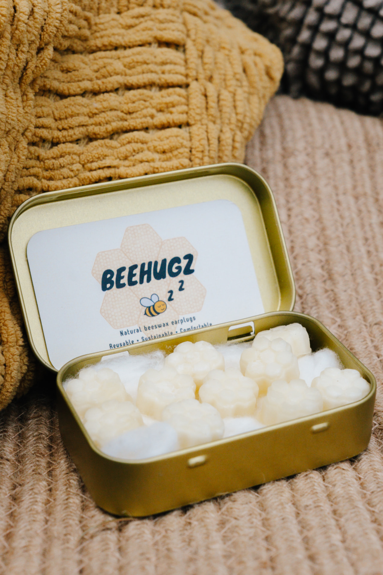 An open gold Beehugz tin filled with honeycomb-shaped beeswax earplugs